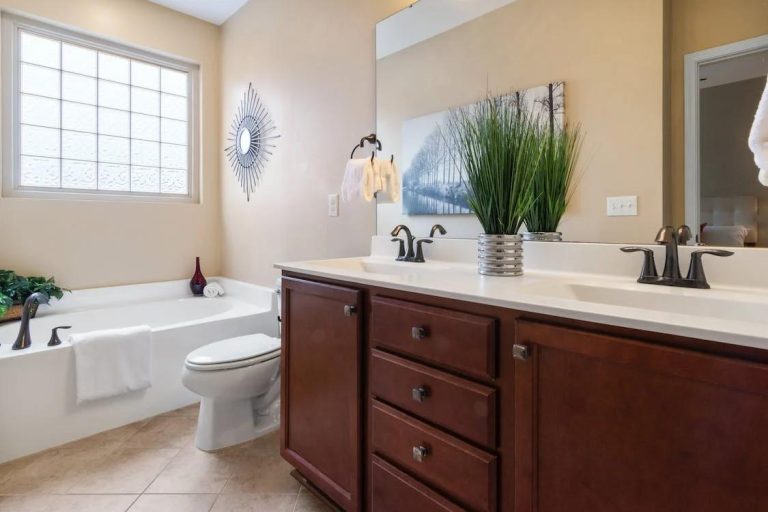 Bai clasice de lux - Tipuri de materiale si finisaje_Baie de lux clasica, cada, corp de mobilier din lemn cu chiuveta, elemente decorative, planta, tablou, perete vopsit cu vopsea de culoare bej, crem.